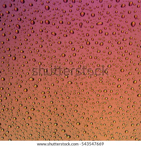 Water drops on a metalic surface with a pink to orange and yellow gradient