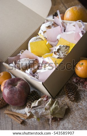 Box with sweets for Christmas. Sweet box with eclairs. Christmas composition from a box cake, tangerine, cinnamon sticks, apples, cones and artificial snow.