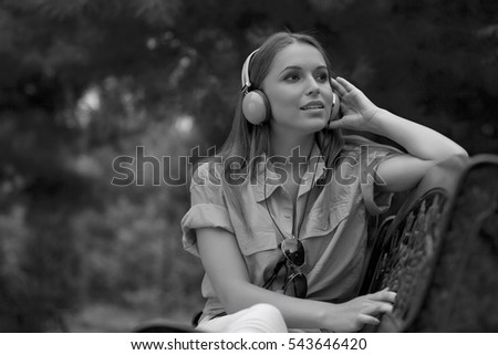 Beautiful young woman listening musing through headphones in park
