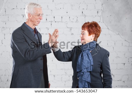 give a high five. Happy smiling old couple standing cuddling together isolated on white brick background. copy space.