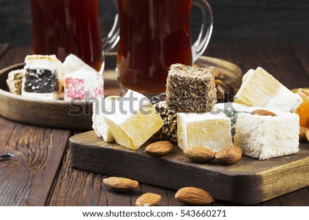 Black tea, oriental sweets, dates and nuts on a dark wooden background