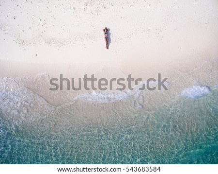 Young woman in a bikini lying on the back on the sand near the waves of blue sea. Top view. Kai island, Andaman Sea, Phuket, Thailand. Aerial Shooting.