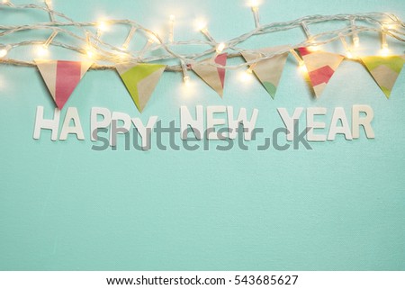 wooden letters word "happy new year" on bright blue background decorated with fairy light and party flag
