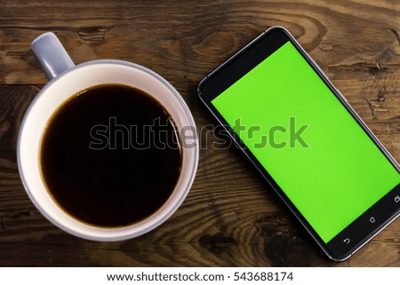Smart phone with green screen on display next to coffee cup, distressed wood table