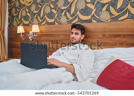 Laptop computer on white bed sheets in cozy room with copy space blank screen. Young businessman.