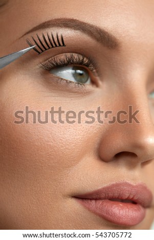 Eyelash Extension. Hand With Tweezers Applying Artificial Eyelashes On Beautiful Woman Eyes. Closeup Of Female Model Face With Long Fake Eye Lashes. Extremely Long Lashes. High Resolution Image