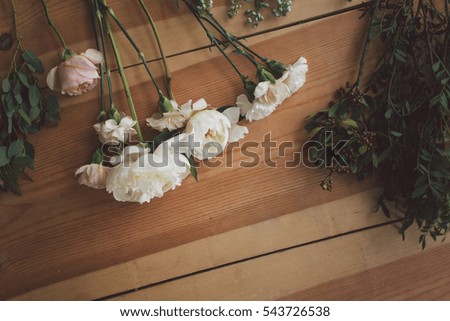 Carnations, roses, peonies and sprigs of greenery on wooden table are prepared for bouquet.