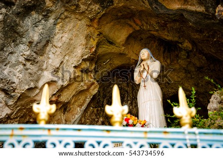 Praying Madonna statue in Notre Dame of Lake grotto near Annecy lake seen through the forging fence. (Duingt, France). 