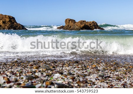 Beautiful sea glass in a variety of colors with blue waves and sky in Fort Bragg, California