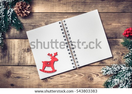 Blank paper notebook on brown wooden table background with branch of a Christmas tree, pine cones and rowan. Top view with copy space.