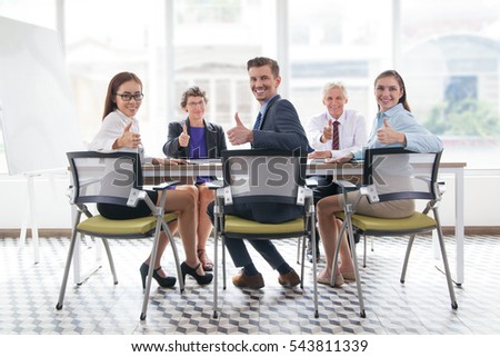 Successful team showing thumbs up at meeting