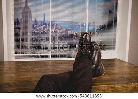 The man sitting in the office with his feet resting on the table and looks out the window of Manhattan on. Relax at lunchtime.