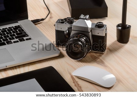 An old camera in the focus of the shot composition. Graphics tablet, computer mouse, modern laptop on the wooden desk for the productive work of a Web designer.