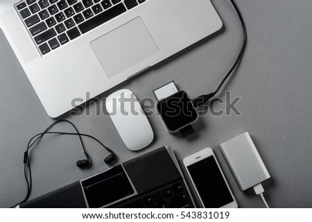 A dream of an every worker is to have such a nice set of technologies at the workplace. Two modern laptops, smartphone, power bank for charging, headphones and computer mouse on a grey desk.