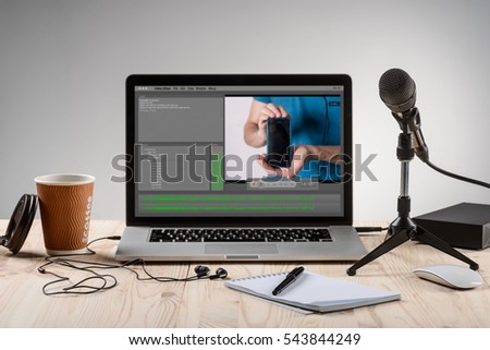 An ordinary workplace of a blogger with a modern laptop and an interface of an application for video editing process. Professional microphone for recording and headphones.