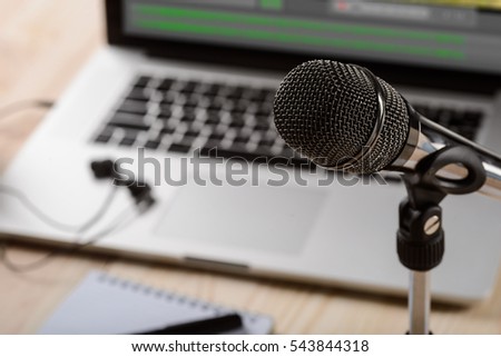 Expensive microphone in the foreground of the camera connected to a holder. Modern laptop and headphones in the blurred background.