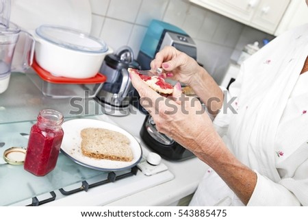 Cropped image of senior woman applying jam on toast in kitchen
