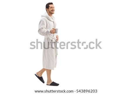 Full length portrait of a young man in a bathrobe holding a cup and walking isolated on white background Royalty-Free Stock Photo #543896203