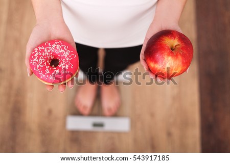 Diet. Woman Measuring Body Weight On Weighing Scale Holding Donut and apple. Sweets Are Unhealthy Junk Food. Dieting, Healthy Eating, Lifestyle. Weight Loss. Obesity. Top View Royalty-Free Stock Photo #543917185