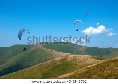 Group of paragliders are flying over the picturesque mountains on a sunny summer day. Paragliding in the Carpathian Mountains in Ukraine.