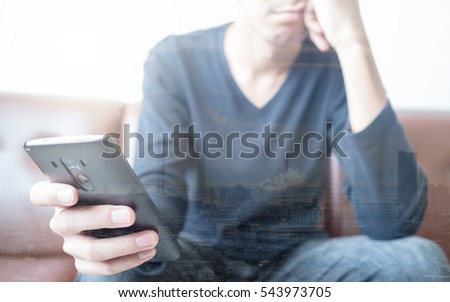 Double exposure of an Asian young man looking at a smart phone in his hand with boring face with his chin on another hand with industrial zone cityscape. Concept of stress / depression / boring