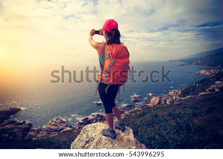 successful hiker use cellphone taking photo on seaside mountain peak rock