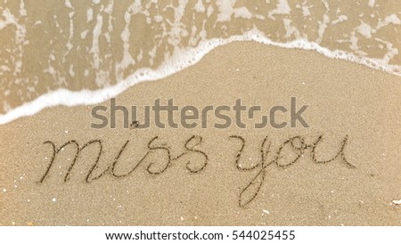 Handwriting words "miss you" on sand of beach