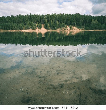 calm lake with reflections of clouds in summer with forest in background - instant vintage square photo