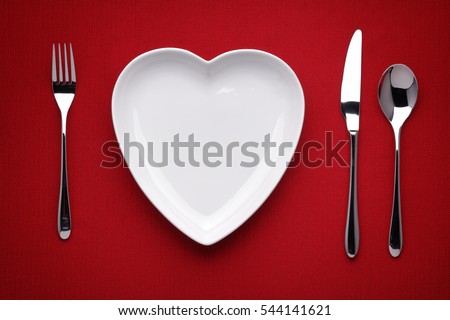 plate in shape of heart, table knife and fork on red  Royalty-Free Stock Photo #544141621