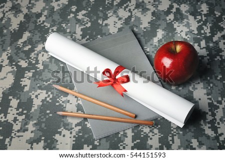 Military education concept. Notebook, pencils, scroll paper and apple on camouflage background