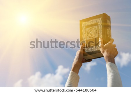 Man's hands holds Koran - holy book of muslims, on blue sky with clouds. With instagram style filter Royalty-Free Stock Photo #544180504