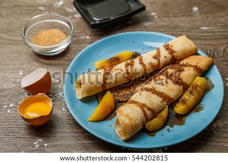 Picture of pancakes with syrup watered with peaches on table with eggs