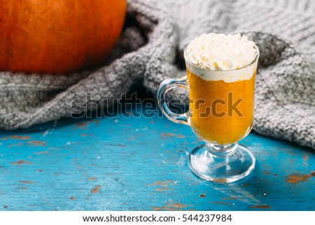Pumpkin spiced latte or smoothie with whipped cream in glass on blue background Autumn or winter hot drink.

