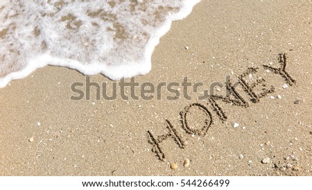 Handwriting words "HONEY" on sand of beach