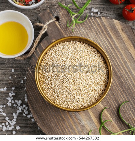 Light cereal quinoa in a metal bowl on a simple wooden background with tomatoes, rosemary, olive oil and salt. Top view