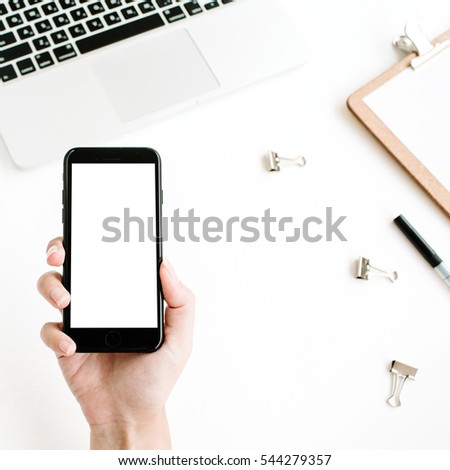 Mockup of mobile phone with blank screen in female hand. Flat lay, top view workspace. Woman entrepreneur hero background with mobile phone