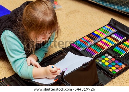 Little girl is drawing using color pencils while laying on floor little girl draws pencils