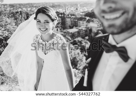 Black and white picture of smiling bride standing behind groom on the hill