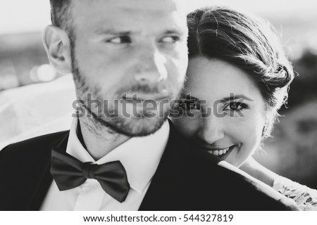 Black and white picture of beautiful happy bride hiding behind broad shoulders of handsome groom