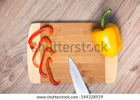 Yellow paprika on cutting board. Red pepper strips and knife whit wood background.