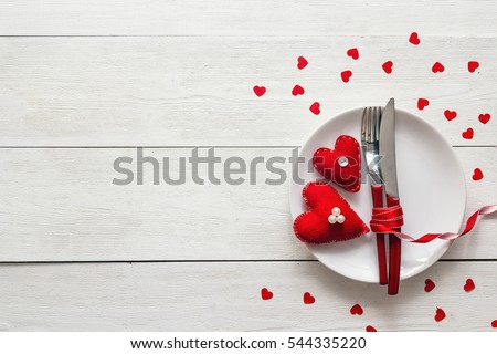 Festive table setting for Valentine's Day with fork, knife and hearts on a white wooden table. Space for text. Top view.
