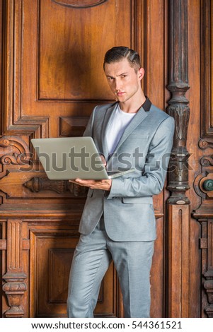 Eastern European Business Man working in New York. Dressing in gray fashionable suit, white undershirt, lawyer standing by vintage office doorway, working on laptop computer.