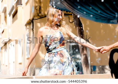 Young girl weared in dress holding her boyfriend's hand and smiling. Couple on a date in sunny summer date