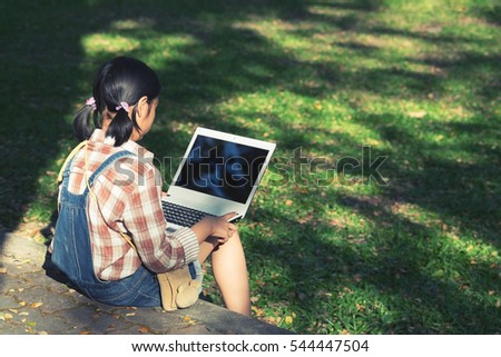 Young school girl wearing colorful outfit using the laptop on a grass field in the park. Back to school, lifestyle, technology young fashion concept, vintage tone.