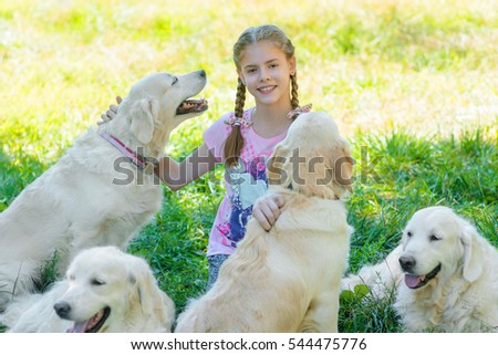 Tired animals and their master after the long walk in the park sit on the juicy grass. Cute girl caresses her dogs and looks right in the camera with fiery eyes.