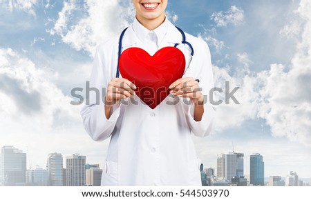 Close view of woman doctor against city background holding red heart