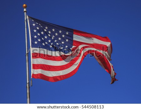 American flag on flagpole waving in the wind against blue sky