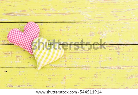 Two homemade fabric hearts on yellow wood background.