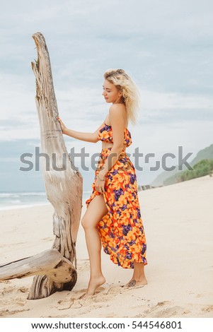 Fashion beauty portrait of white girl with blonde curly hair wearing tropical print top and skirt on the beach shore