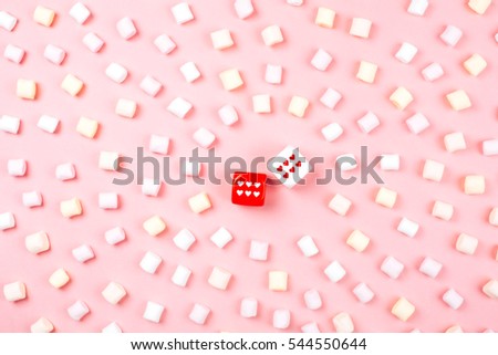 Dice with hearts and rows of marshmallow on pink background. Love game concept. Flat lay style.